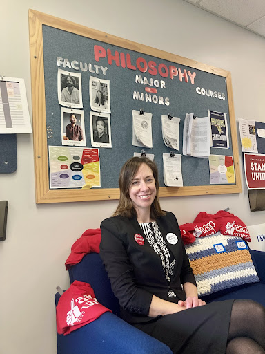 AAUP-Utica President Leonore Fleming posing outside of the Philosophy department bulletin board.