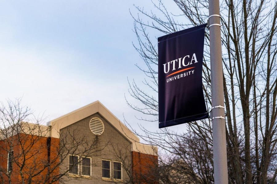 Utica University sign hangs on a pole across from a residential building. 