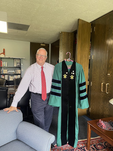 Dr. Todd Pfannestiel displays his green doctoral robe from the College of William and Mary. Three stripes on the sleeves represent a Doctorate degree, the blue piping represents his PhD in Arts and Sciences, the W and M script seal, a Utica seal, a Clarion pin, a Phi Beta Kappa pin and a Utica moose.