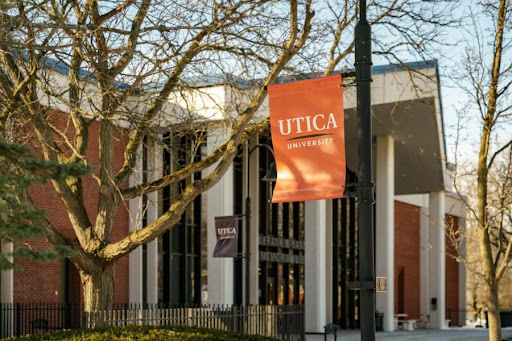 The Utica University flag hangs on a pole in front of the Frank E. Garnett library.  