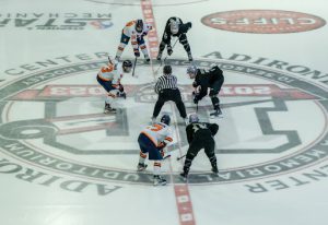Three Utica mens ice hockey players square up at center ice.