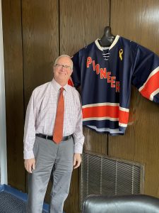 President Pfannestiel next to his Utica Hockey jersey displayed in his office. He will step away from the leadership role on Dec. 31. Photo by Megan Wright.