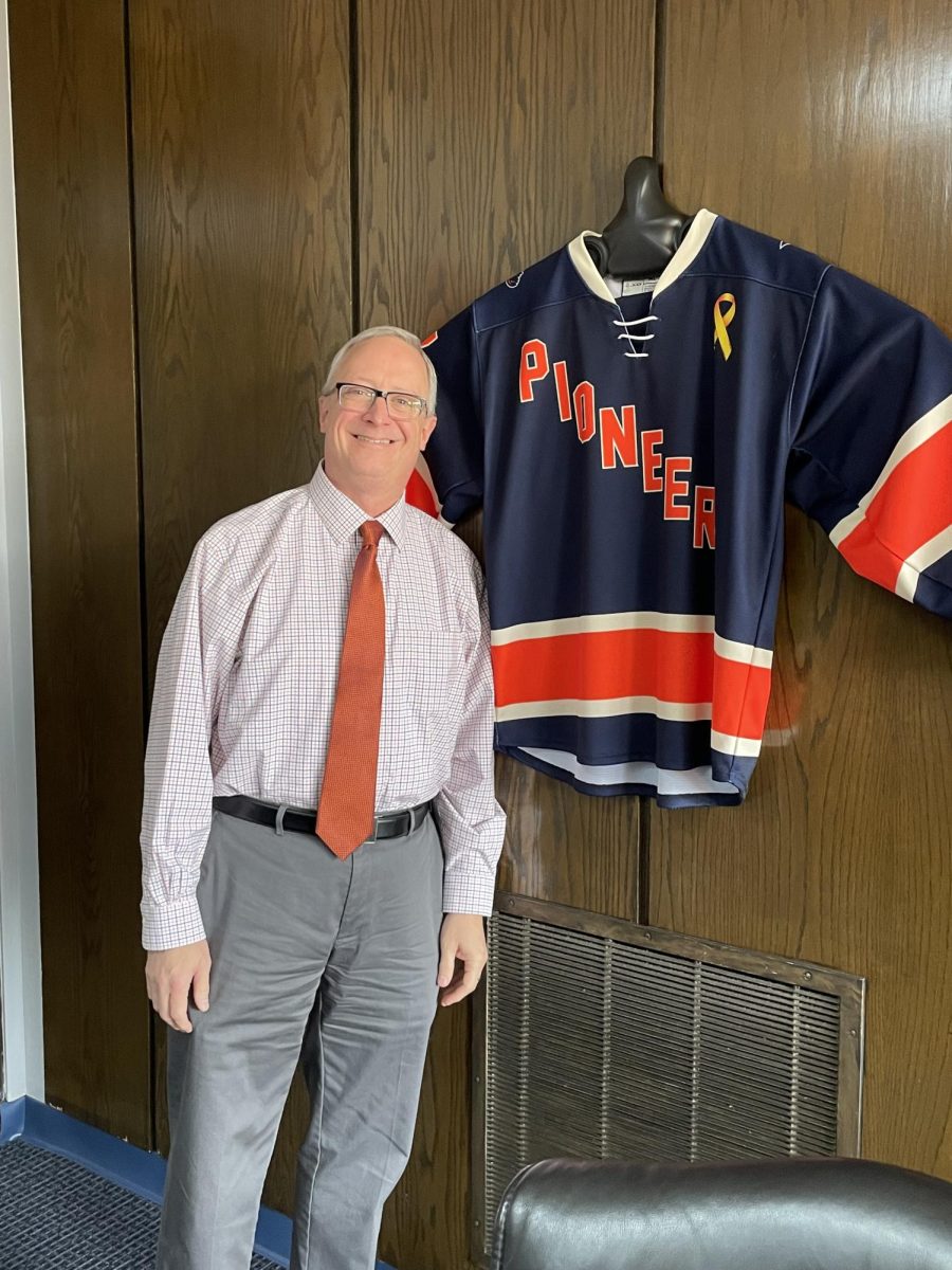 President Pfannestiel next to his Utica Hockey jersey displayed in his office. He will step away from the leadership role on Dec. 31. Photo by Megan Wright.